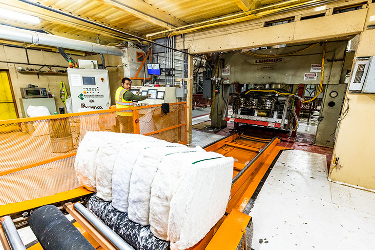 Employee monitors as lint is pressed into bales, sampled for grading and wrapped in plastic for shipping.