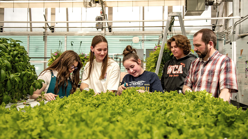 Four high school students and teacher in a greenhouse