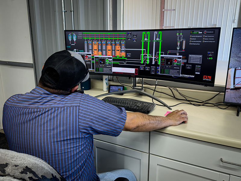  A man at a desk with computer screens showing grain levels in silos.