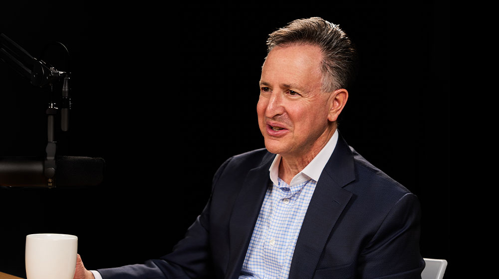 Man sitting in a studio beside a microphone and holding a coffee mug