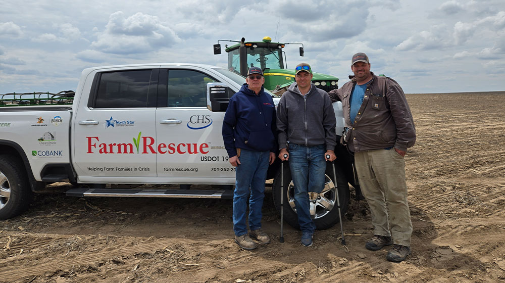 Three men in a field by a truck, tractor and planter